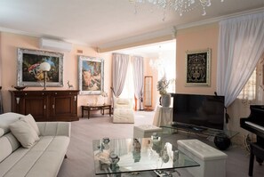 A living room with a sofa, a glass coffee table, a television, a piano, and framed artwork on the walls. - Villa Blondie in Castellammare del Golfo (Castellammare del Golfo)