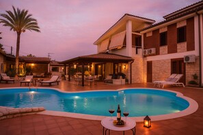 A swimming pool with lounge chairs and a table with wine glasses and bottles, surrounded by a patio area with a palm tree and a building with a balcony. - Villa Blondie in Castellammare del Golfo (Castellammare del Golfo)