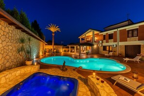 En swimmingpool med ett bubbelbad, solstolar och en stenmur.