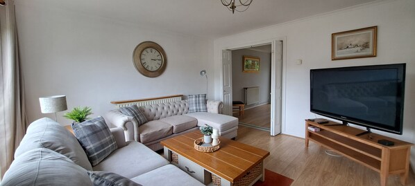 Een woonkamer met een bank, salontafel, televisie en een klok aan de muur.