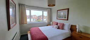 Een hotelkamer met een bed, nachtkastje, lamp, een ingelijste foto en een raam met gordijnen.