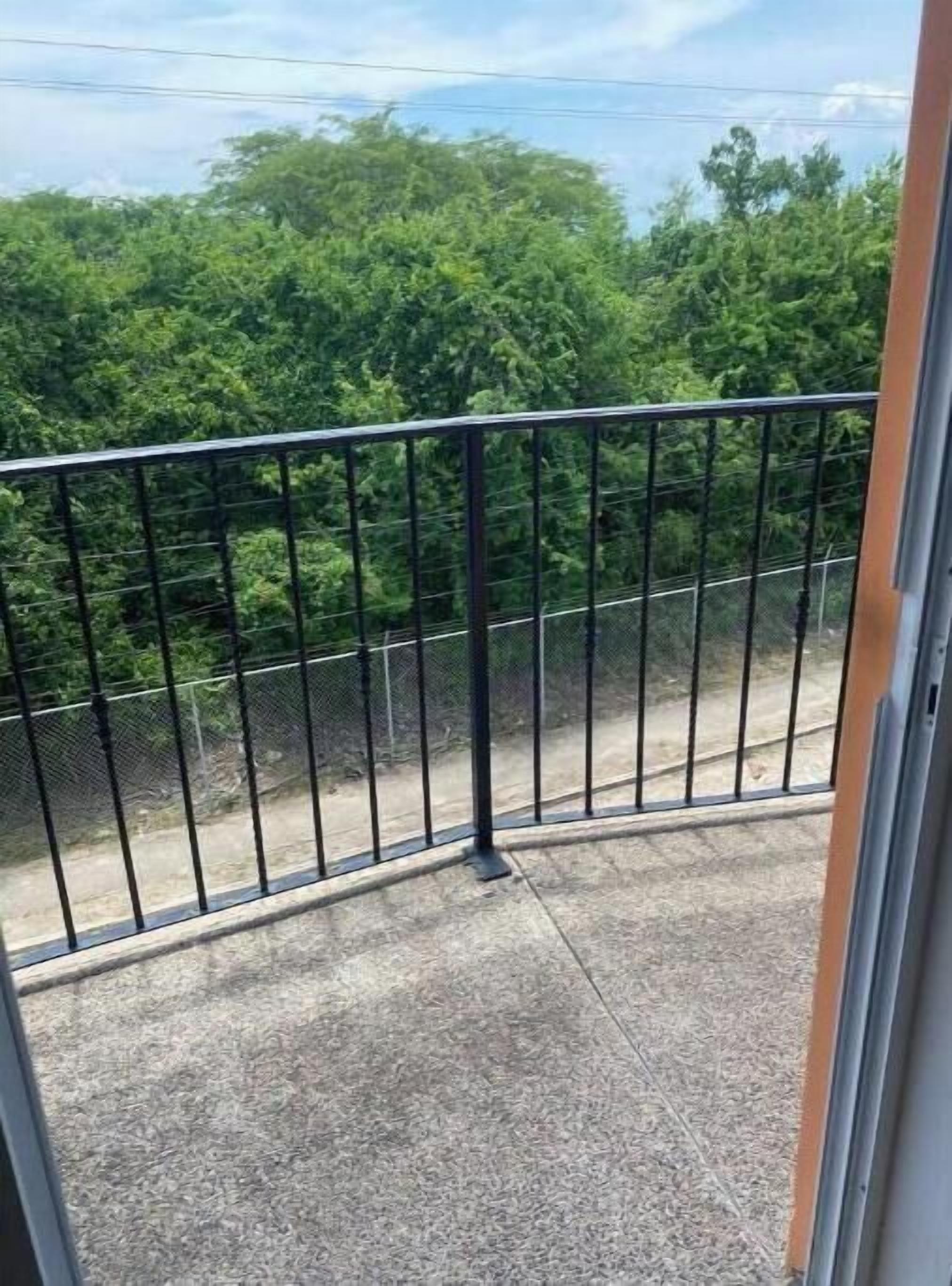Un balcon doté d’une rambarde en métal donnant sur une zone en béton et une végétation luxuriante.