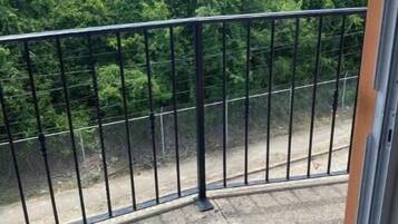 Un balcon doté d’une rambarde en métal donnant sur une zone en béton et une végétation luxuriante.