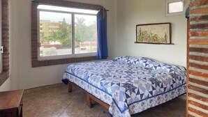 Une chambre à coucher avec un lit, un ventilateur de plafond, une fenêtre avec des rideaux et un tableau encadré au mur.