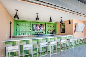 Un espace bar aux couleurs vert et blanc, agrémenté de plusieurs suspensions et de diverses bouteilles exposées sur des étagères.
