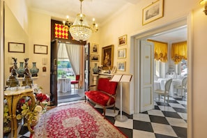 A hallway with a red velvet chair, a chandelier, framed pictures, and a checkered floor.