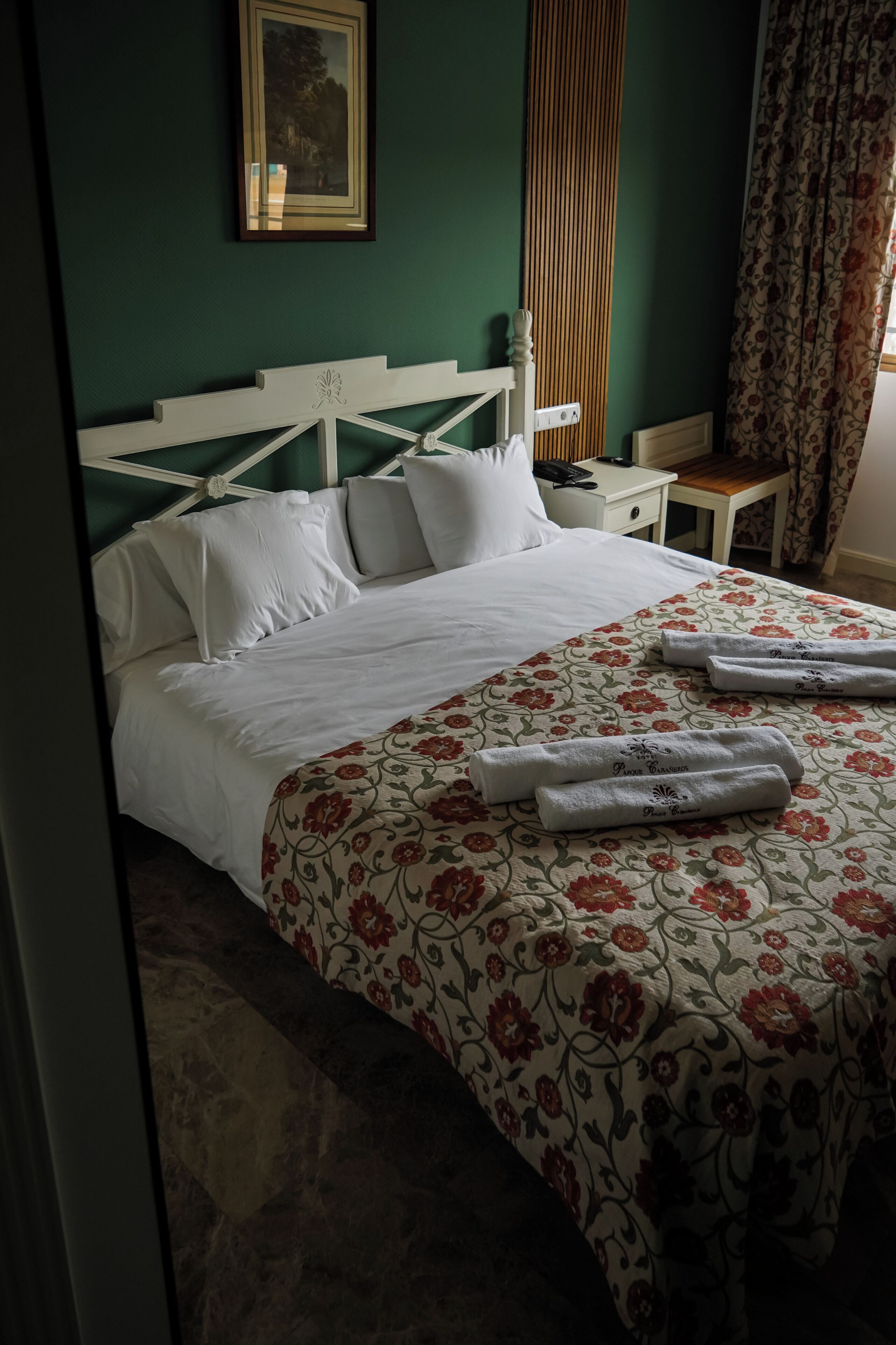 Una cama bien hecha con una colcha estampada con motivos florales, una mesita de noche con una lámpara y un cuadro en la pared.