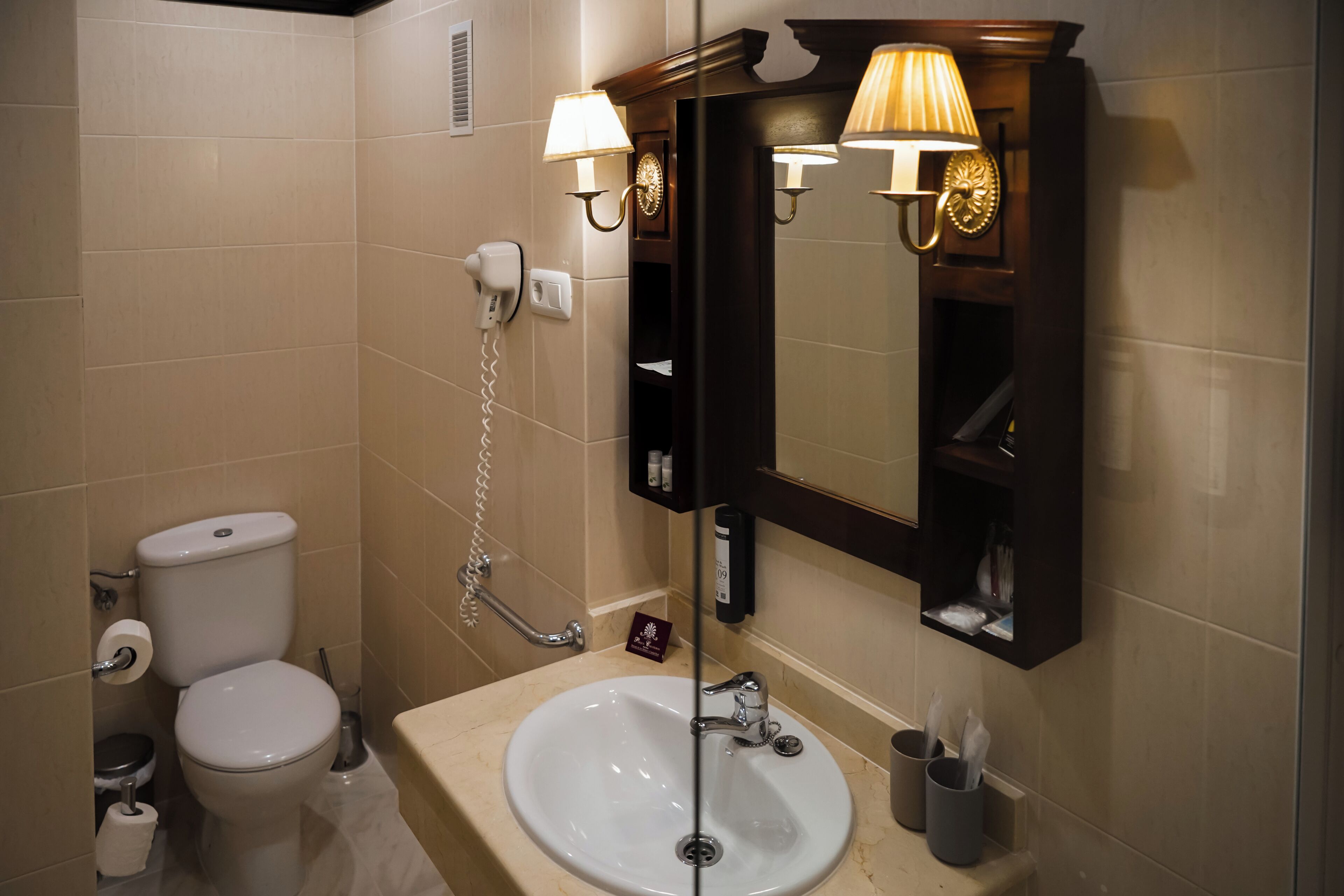 Une salle de bain équipée de toilettes, d’un lavabo et d’un miroir, le tout agrémenté d’appliques murales.