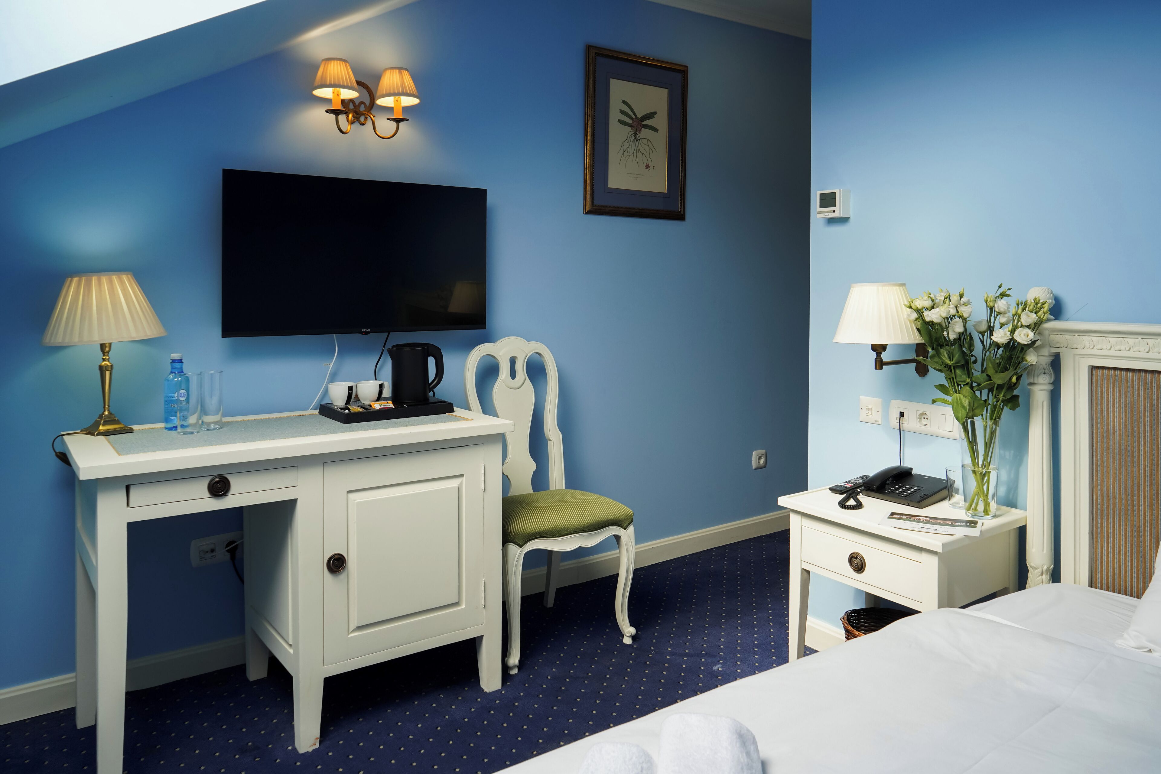 Ein Hotelzimmer mit Schreibtisch, Stuhl, Bett, Fernseher und einer Vase mit Blumen.
