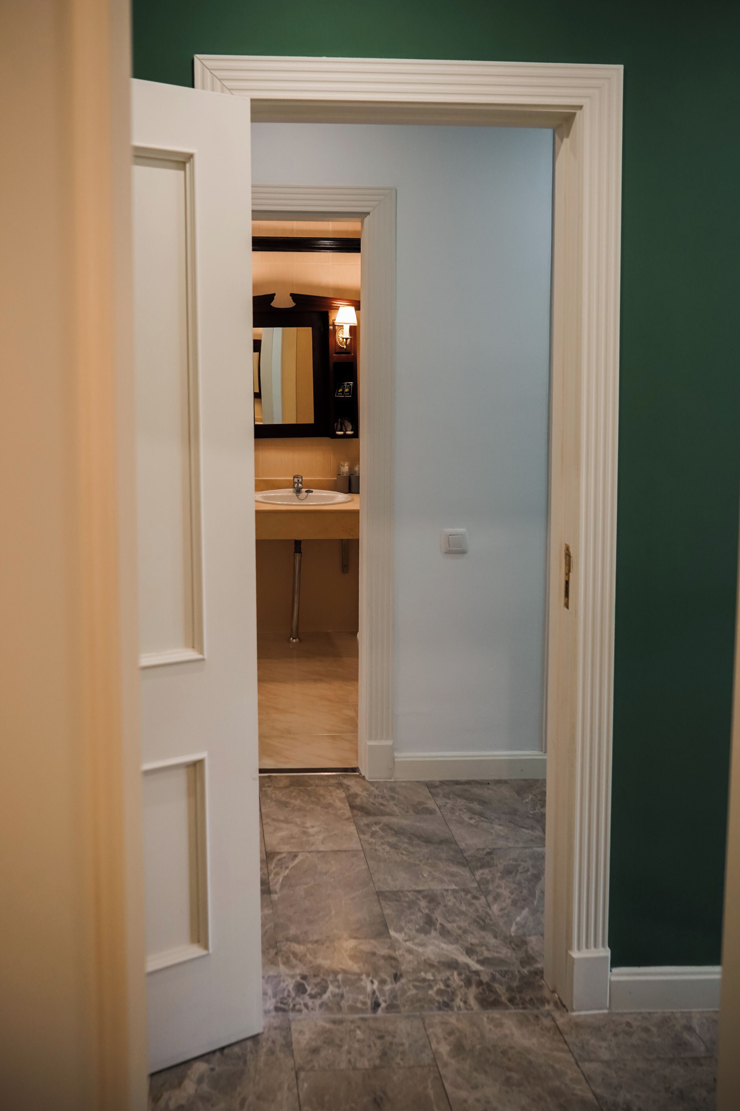 A hallway leading to a bathroom with a sink and mirror.