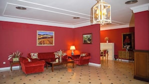 A room with a red wall, a chandelier, a sofa set, and a fireplace. - NUEVO HOTEL PARQUE CABAÑEROS (Horcajo de los Montes)