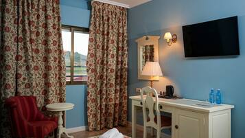 A hotel room with a bed, two chairs, a desk, a television, a lamp, and a window with curtains.
