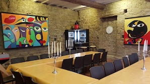 A dining area with a long table covered in yellow tablecloths, surrounded by chairs. There are paintings on the walls, a clock, and a television on a stand. - Spacious 8-bedroom country house in Villepinte with private pool and parking (Villepinte)