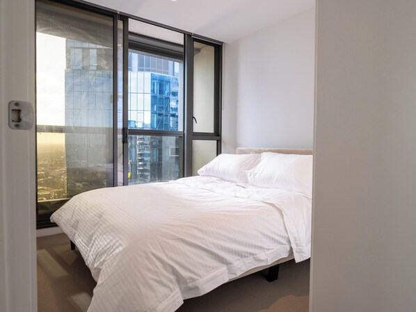 A bedroom with a bed, a window, and a view of buildings.
