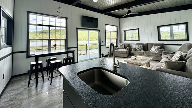 A modern kitchen with a large island, dining area with chairs, and a living room with sofas.