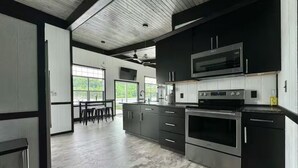 A modern kitchen with dark cabinetry, stainless steel appliances, and a large window providing natural light.