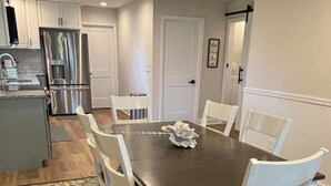 A dining area with a dark wooden table and white chairs, a kitchen with stainless steel appliances, and a door leading to another room. - Beautiful 2-bedroom water view house in Annapolis (Annapolis)