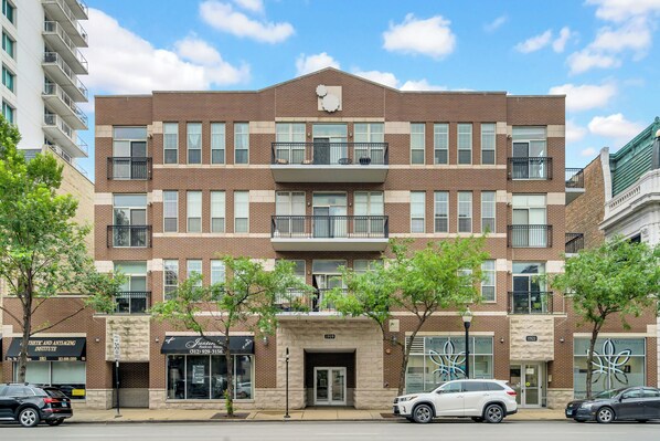 A multi-story brick building with a central entrance, balconies, and storefronts on the ground floor.