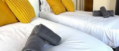 Ein Hotelzimmer mit zwei Betten, jeweils mit weißer Bettwäsche und dunklen Kopfteilen. Auf den Betten liegen gelbe und graue Handtücher.