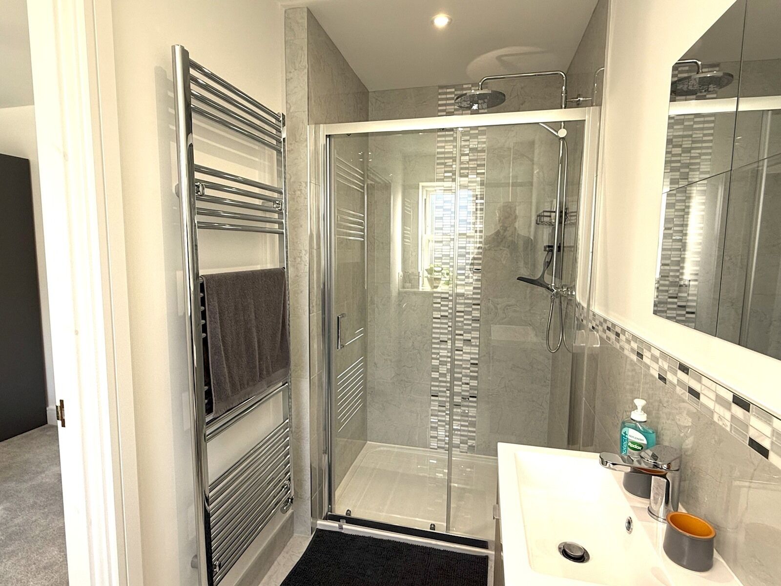 A modern bathroom with a glass-enclosed shower, a white sink with a soap dispenser, and a towel rack.