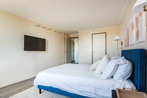 A hotel room with a bed, a flat-screen TV mounted on the wall, and a door leading to another room.