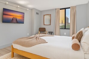 Une chambre d’hôtel moderne avec un grand lit, une vue sur la ville et une peinture représentant un coucher de soleil accrochée au mur.