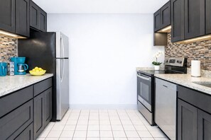 Une cuisine moderne avec des meubles de couleur sombre, un réfrigérateur en acier inoxydable, une machine à café et un bol de citrons.