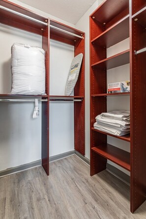 A walk-in closet with wooden shelving, a hanging rack, and a folded ironing board.