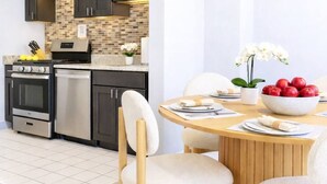 Een moderne keuken met donkere kastjes, een betegelde achterwand, roestvrijstalen apparatuur en een eethoek met een houten tafel en stoelen.