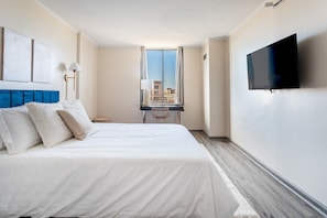 A hotel room with a bed, a desk, a chair, a TV, and a window with a city view.