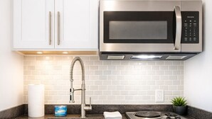 A kitchen with white cabinets, a stainless steel microwave, a sink with a faucet, a stove, and a dishwasher.