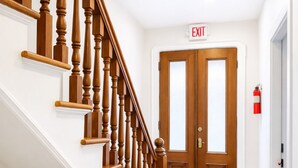 A wooden staircase with a white wall and a door with an exit sign.