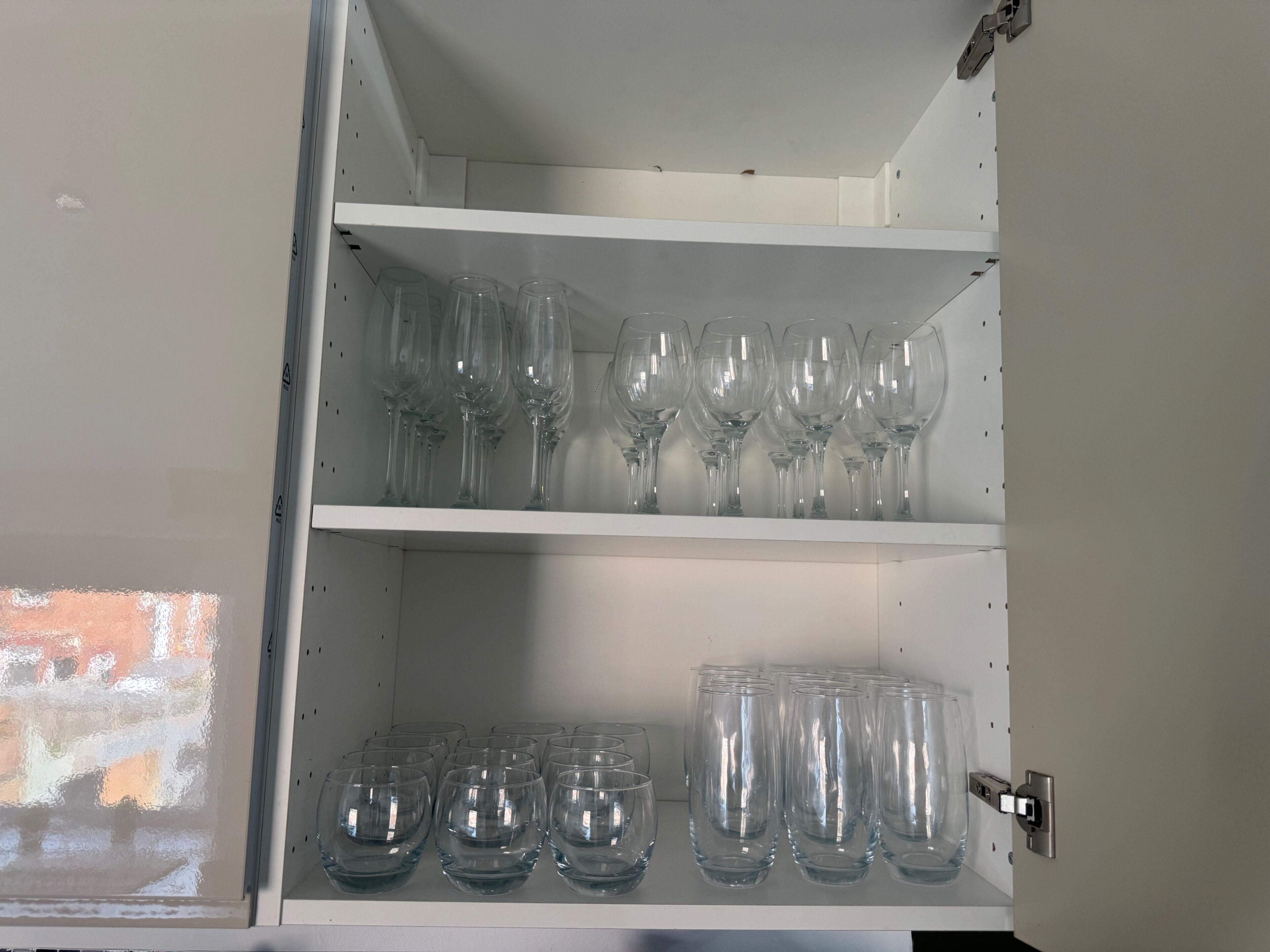Un armario blanco con estantes que contienen varios vasos de vidrio transparente.