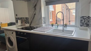 A modern kitchen with a built-in washing machine, a stainless steel sink, and a window with a view of the street. - Apt-sleeps 6-parking-ideal for Contractors-garden (Newcastle-upon-Tyne)