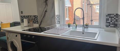 Una cocina moderna con lavadora integrada, un lavamanos de acero inoxidable y una ventana con vistas a la calle.