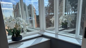 A room with a large window, a potted orchid, and a view of trees and buildings outside. - Apt-sleeps 6-parking-ideal for Contractors-garden (Newcastle-upon-Tyne)