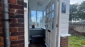 A narrow entryway with a white door, a small bench, and a window with a view of the sky and greenery. - Apt-sleeps 6-parking-ideal for Contractors-garden (Newcastle-upon-Tyne)