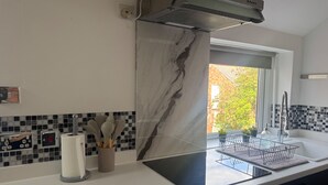 A modern kitchen with a built-in stove, a window with a view of greenery, and a backsplash with black and white tiles. - Apt-sleeps 6-parking-ideal for Contractors-garden (Newcastle-upon-Tyne)