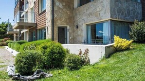 Un edificio moderno de varios pisos con fachada de piedra y madera, balcones y un jardín bien cuidado.