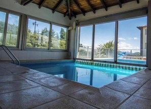 An indoor swimming pool with large windows, tiled flooring, and a wooden ceiling. - Lake Department I (San Carlos de Bariloche)