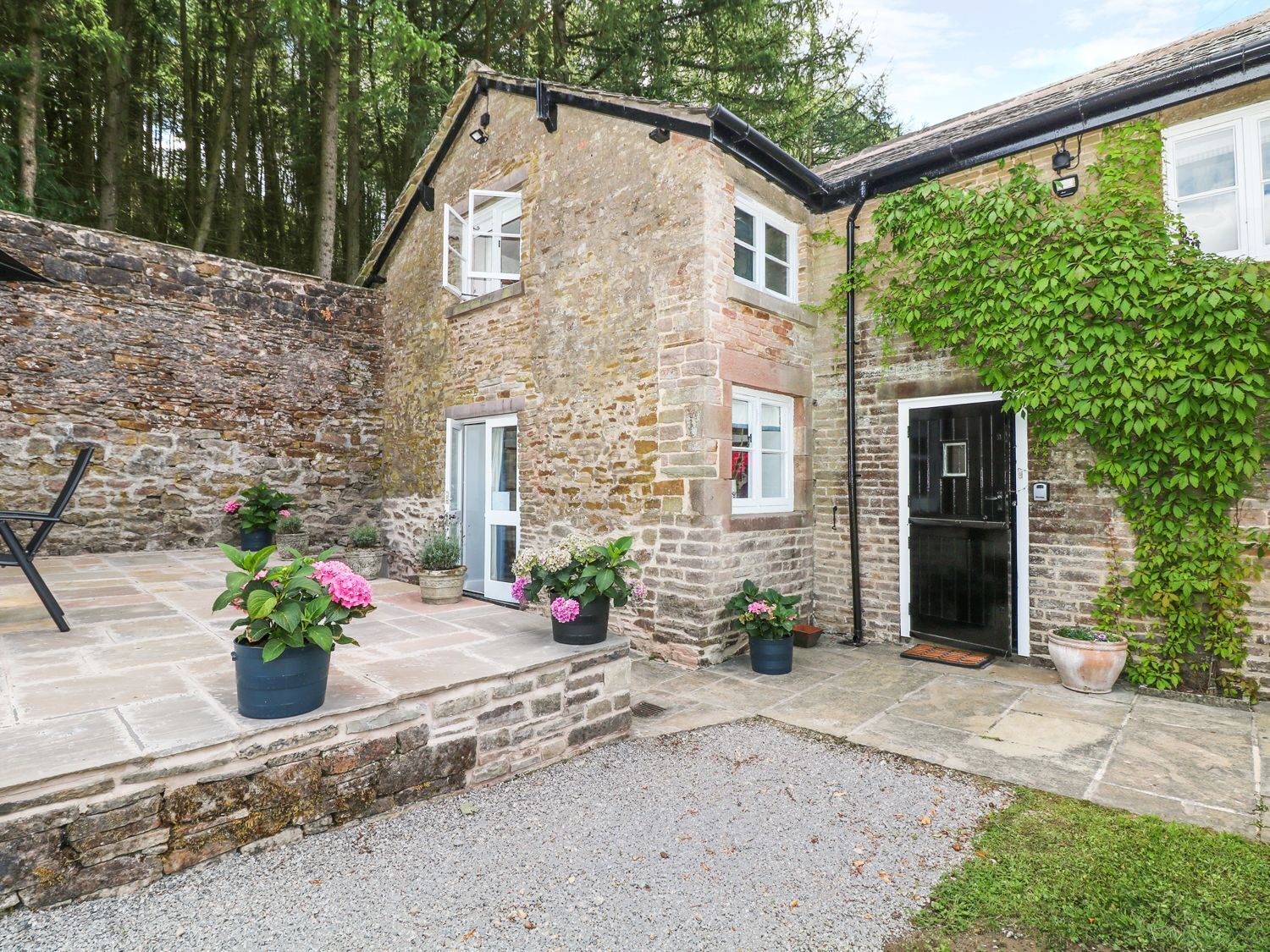A stone building with a door, windows, and a small garden area with potted plants.
