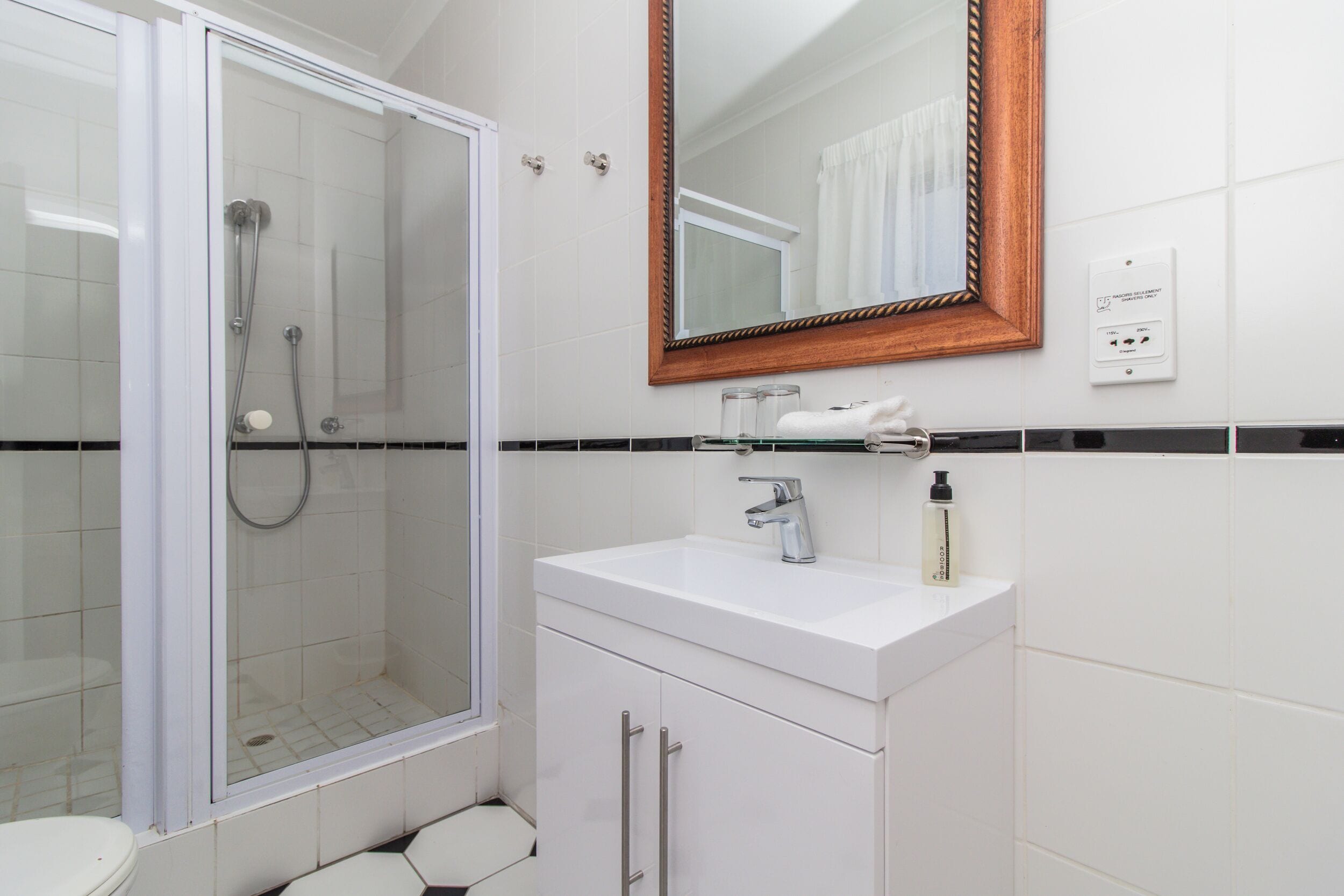 Un baño con ducha envuelta en vidrio, un lavamanos blanco con un espejo arriba y un inodoro.