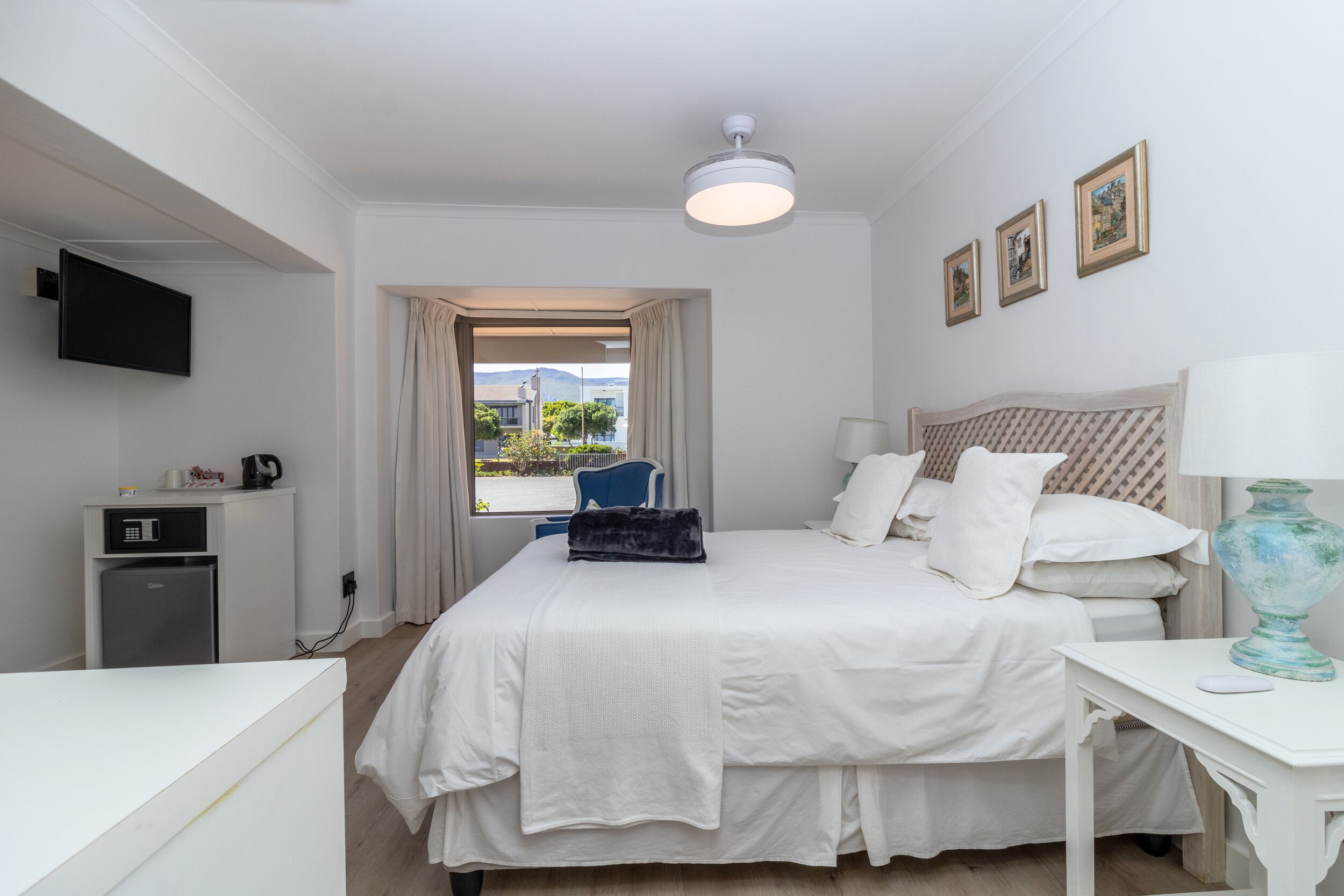 Ein Hotelzimmer mit Bett, Schreibtisch, Fernseher, kleinem Kühlschrank und einem Fenster mit Vorhängen.