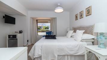 Ein Hotelzimmer mit Bett, Schreibtisch, Fernseher, kleinem Kühlschrank und einem Fenster mit Vorhängen.