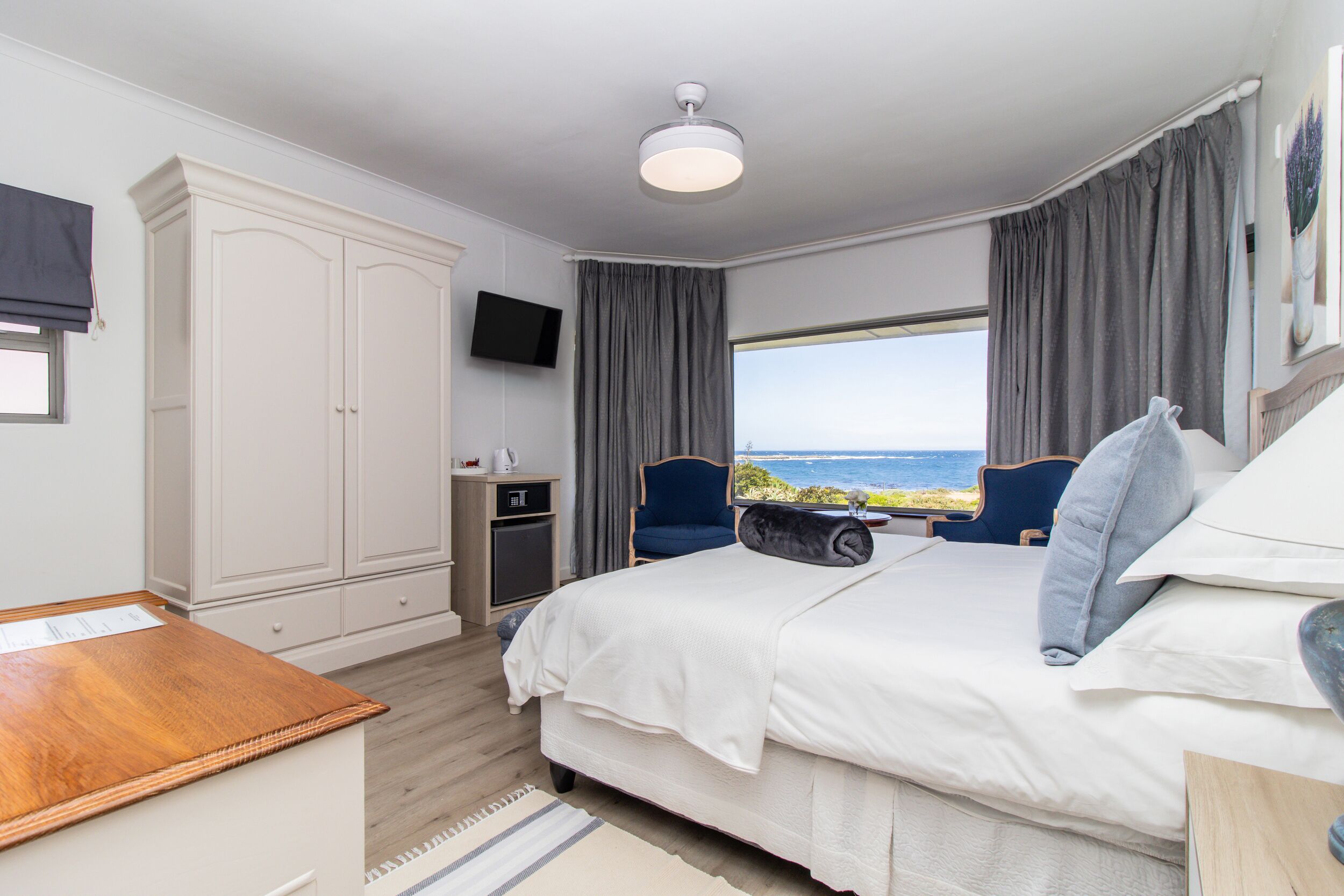 Ein Schlafzimmer mit einem großen Bett, einem Schreibtisch, einem Kleiderschrank, einem Fernseher und Meerblick.