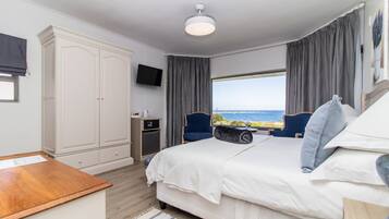 Ein Schlafzimmer mit einem großen Bett, einem Schreibtisch, einem Kleiderschrank, einem Fernseher und Meerblick.