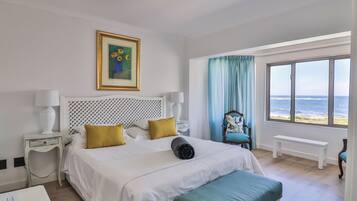Un cuarto de hotel con una cama, un banco, una silla, una ventana con vista al mar y un cuadro en la pared.