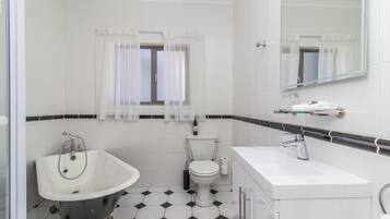 A bathroom with a bathtub, toilet, and sink, featuring a black and white tiled floor and a window with sheer curtains.