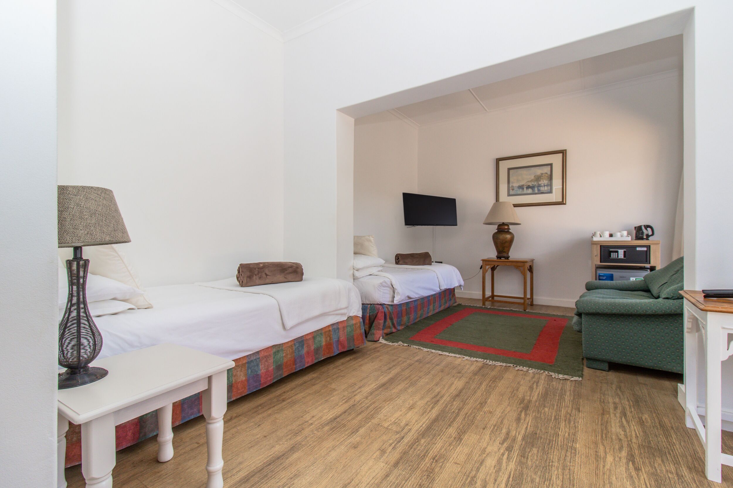 Ein Hotelzimmer mit zwei Betten, einem Fernseher, einer Lampe, einem kleinen Tisch, einem grünen Sofa und Holzboden.