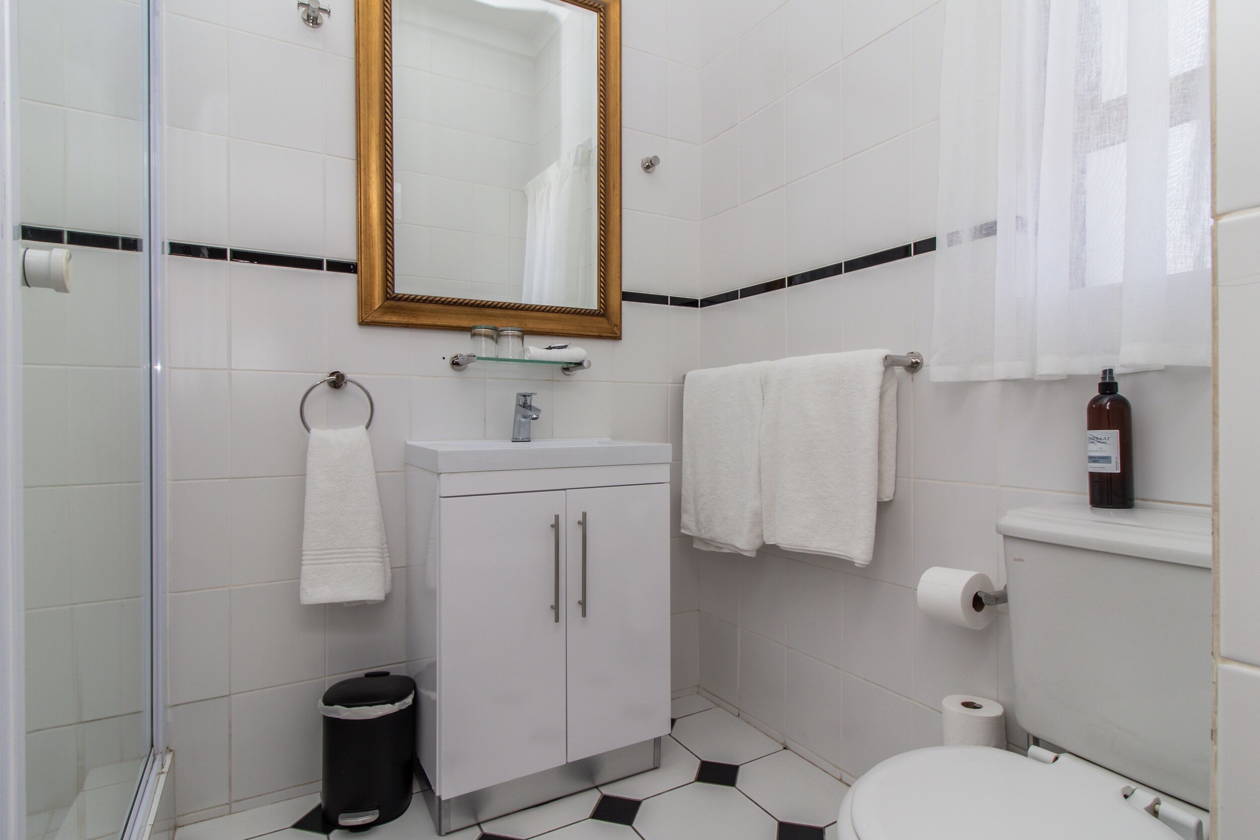 A bathroom with a white sink, a mirror, a toilet, and a trash bin.